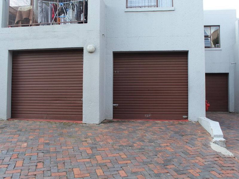 Exterior view of a residential apartment complex featuring multiple brown roller shutter garage doors and a paved driveway area.
