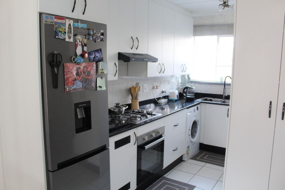 A functional galley-style kitchen featuring white cabinetry, dark countertops, a gas hob, built-in oven, and integrated laundry plumbing.