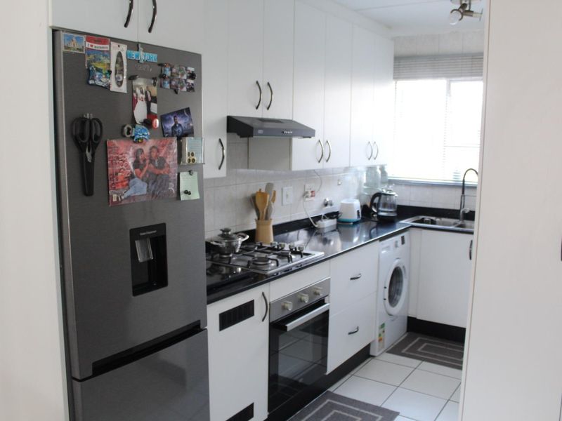 A functional galley-style kitchen featuring white cabinetry, dark countertops, a gas hob, built-in oven, and integrated laundry plumbing.