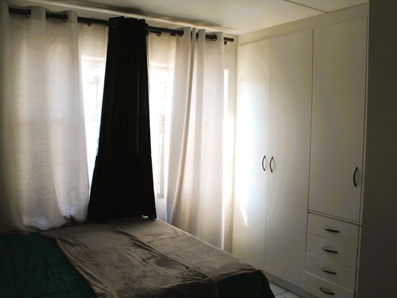 A bedroom featuring white built-in cupboards with integrated drawer storage and large windows with curtain treatments.