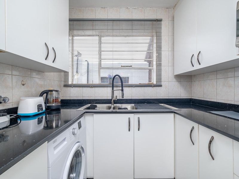 Compact kitchen featuring white cabinetry, dark stone countertops, a double bowl sink, and an integrated washing machine.
