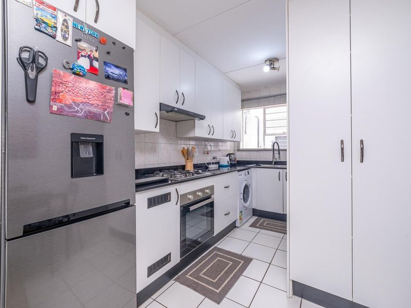 A functional galley-style kitchen featuring white cabinetry, dark countertops, a gas hob, built-in oven, and tiled flooring with integrated laundry appliance space.