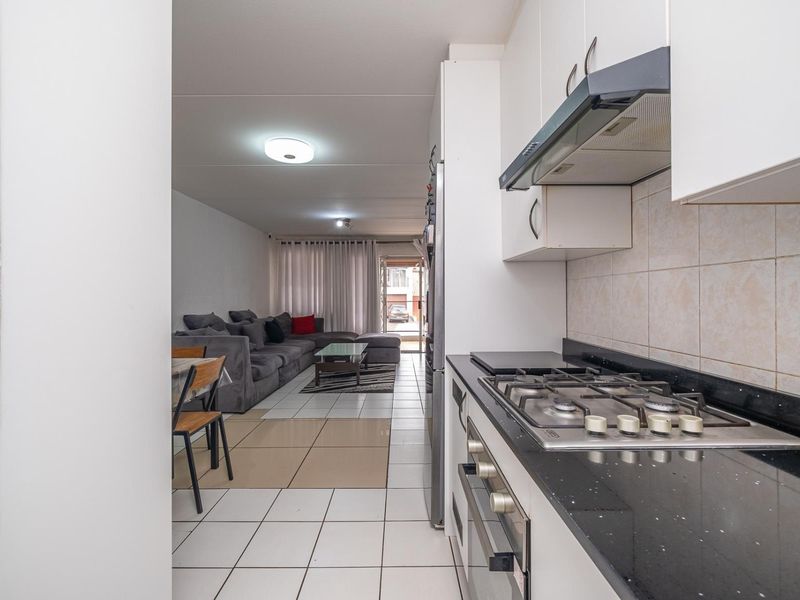Open-plan kitchen and living area featuring tiled flooring, built-in cabinetry, and integrated gas hob with extractor fan, creating a functional and connected living space.