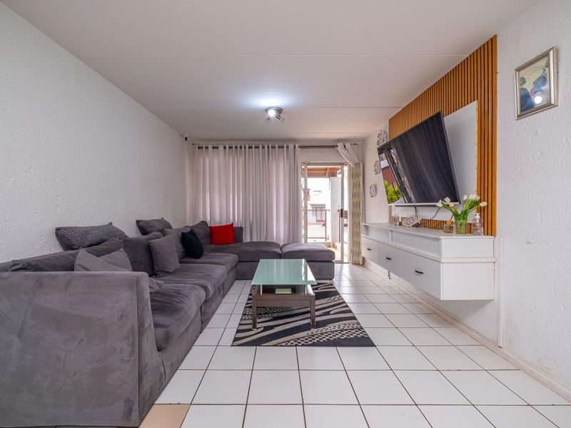 A well-maintained living room featuring tiled flooring, a decorative slat wood feature wall, and a floating media console with access to a balcony.