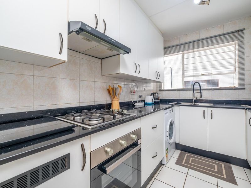 A functional kitchen featuring white cabinetry, black granite countertops, a gas hob, built-in oven, and integrated laundry plumbing.