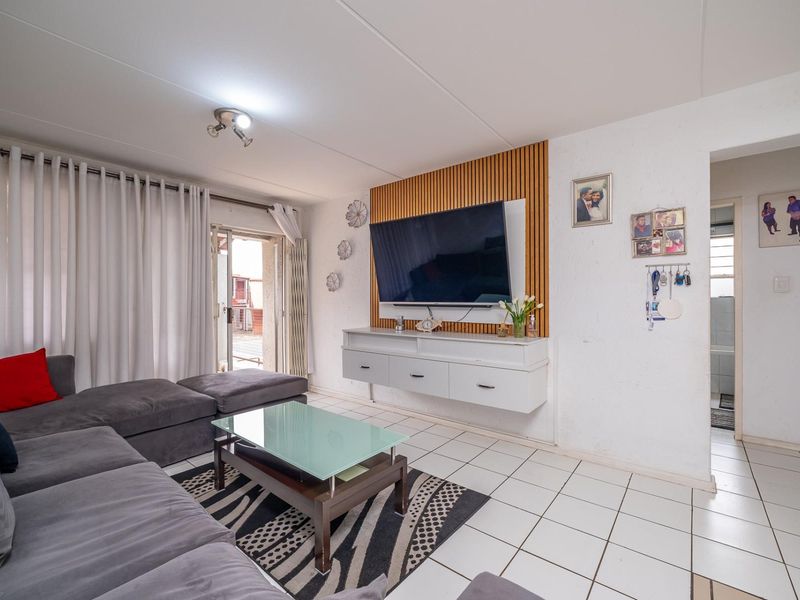 Living room featuring tiled flooring, a slatted wood feature wall with a mounted media console, and access to an outdoor area via sliding doors.