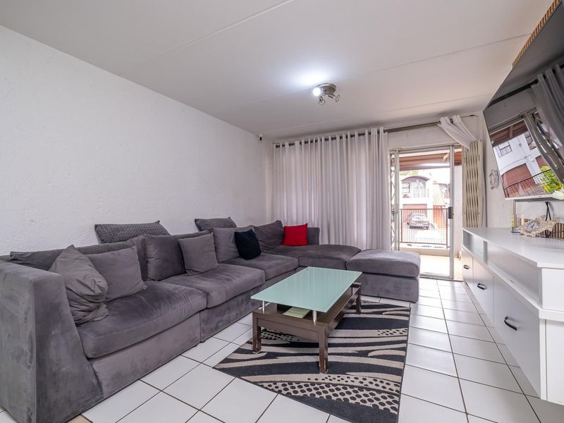 A bright living room featuring tiled flooring, a built-in media console, and direct access to an outdoor patio area through a sliding glass door.