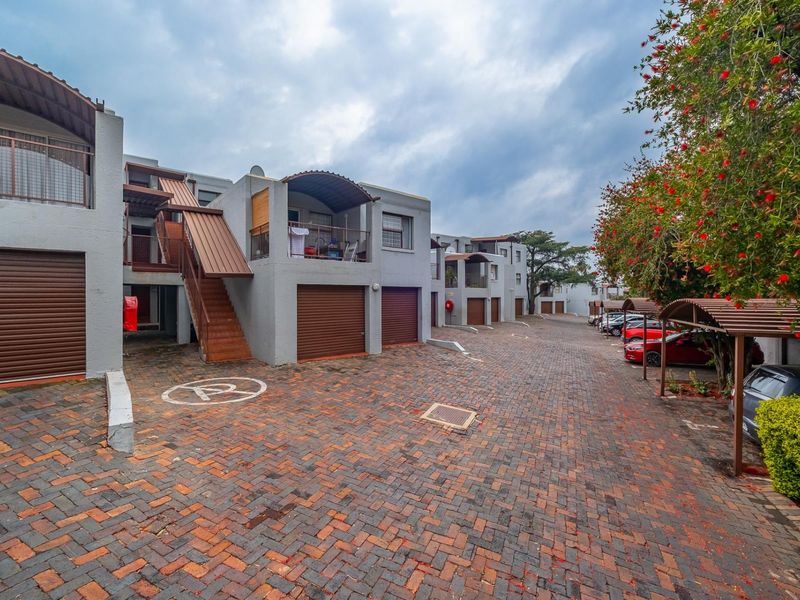 Exterior view of an apartment complex featuring brick paved driveways, individual garage units, and covered balconies with external staircases.