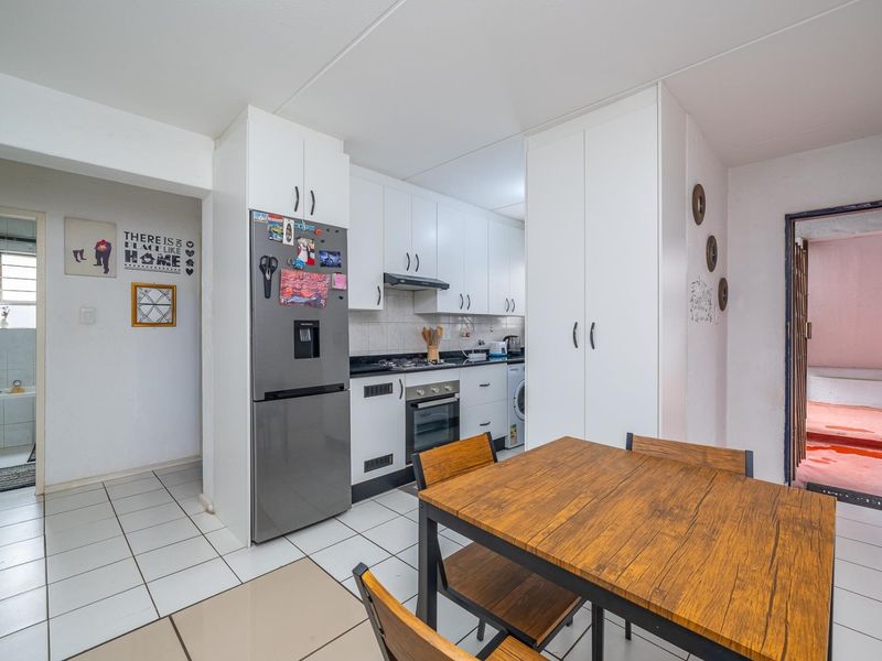 A functional kitchen featuring white cabinetry, built-in oven and hob, and tiled flooring, with an adjacent dining area and access to a bathroom.