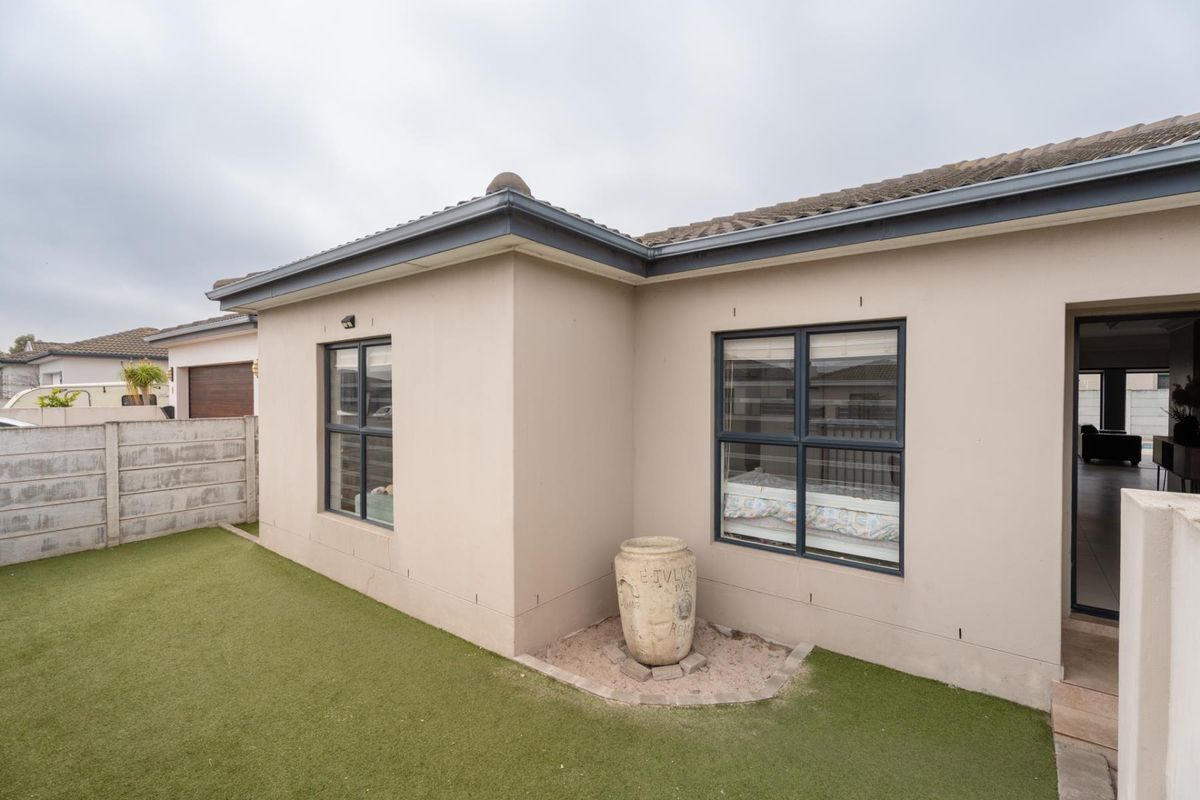 Rear view of the house featuring a low-maintenance artificial lawn, concrete boundary wall, and modern aluminium window frames.
