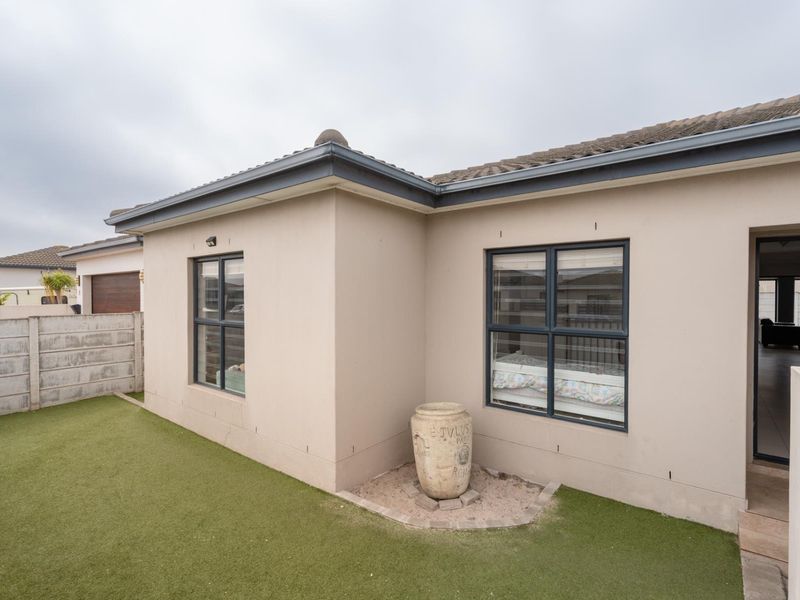 Rear view of the house featuring a low-maintenance artificial lawn, concrete boundary wall, and modern aluminium window frames.