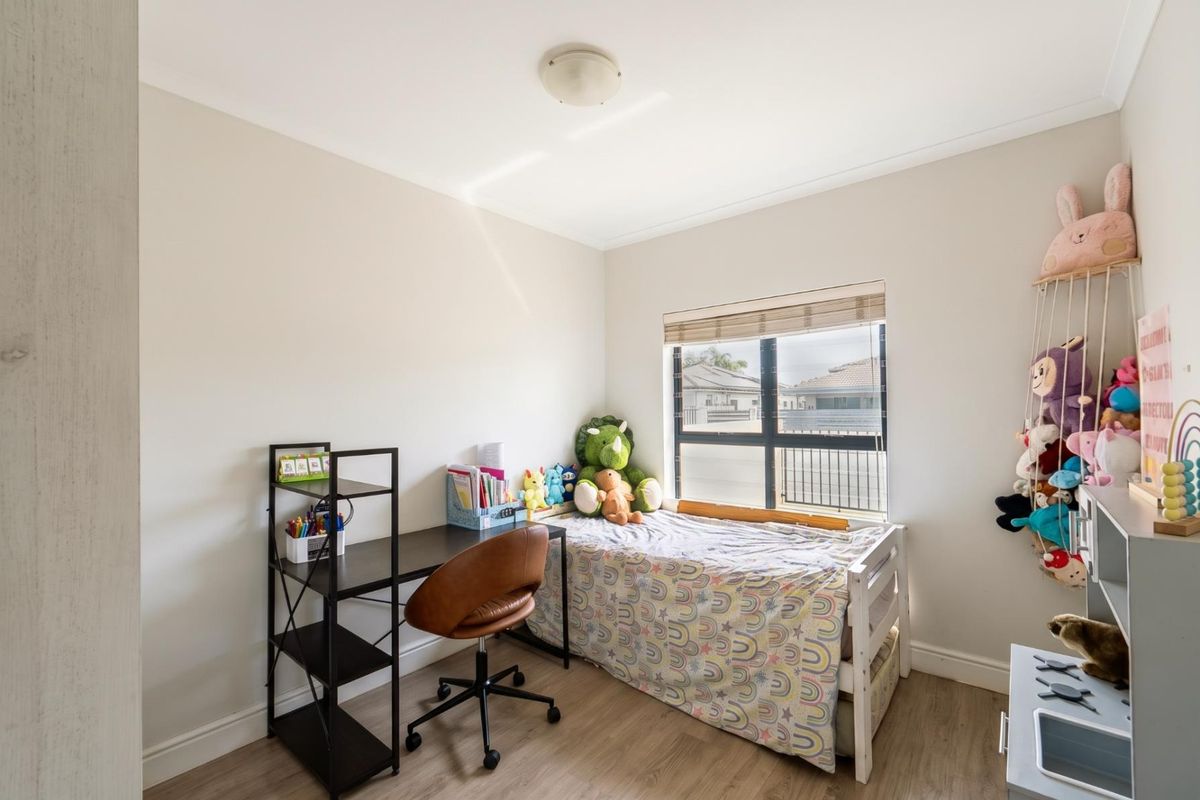 A well-lit bedroom featuring neutral walls, wood-look flooring, and a window with fitted blinds.