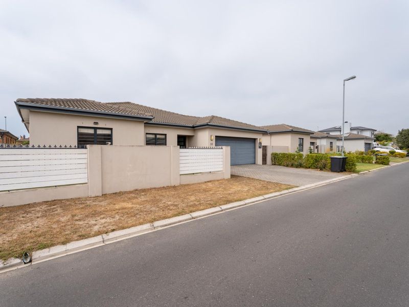 Front exterior view of a modern single-story house featuring a tiled roof, paved driveway, and secure boundary wall with integrated garage.