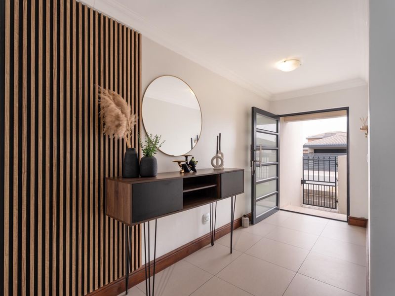 A bright and modern entrance hall featuring stylish vertical timber wall paneling, neutral floor tiles, and a contemporary glass-panelled front door.