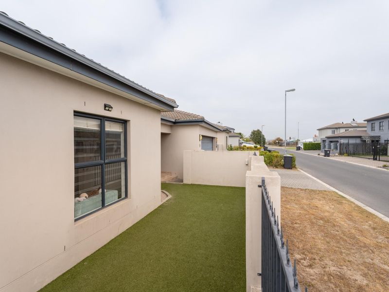 Front exterior view of the property featuring a low-maintenance artificial turf lawn, perimeter metal fencing, and modern neutral-toned facade with aluminium window frames.