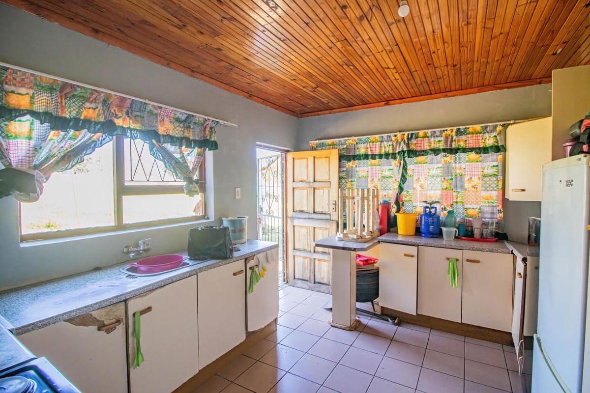 A functional kitchen featuring tiled floors, built-in cabinetry with stone-look countertops, a stainless steel sink, and a timber ceiling.