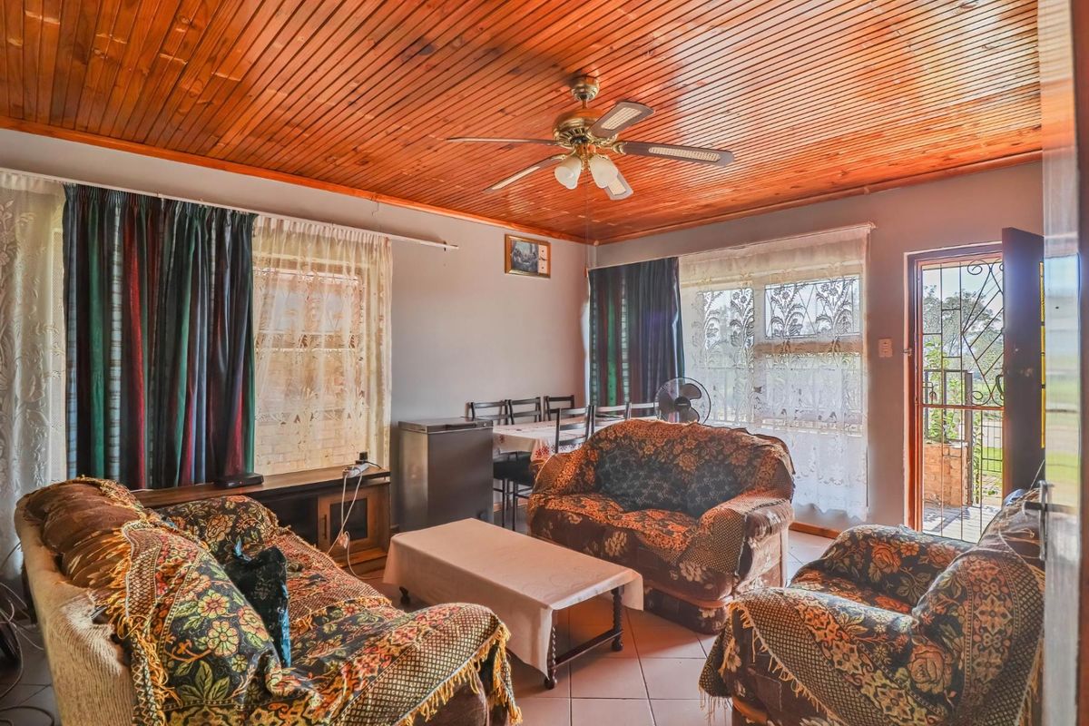A living room featuring a timber tongue and groove ceiling, ceiling fan, tiled flooring, and direct access to the exterior via a security gate.
