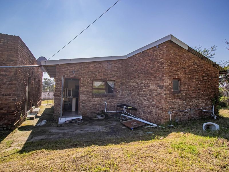Rear view of a brick house featuring an exposed concrete apron and external plumbing fixtures.