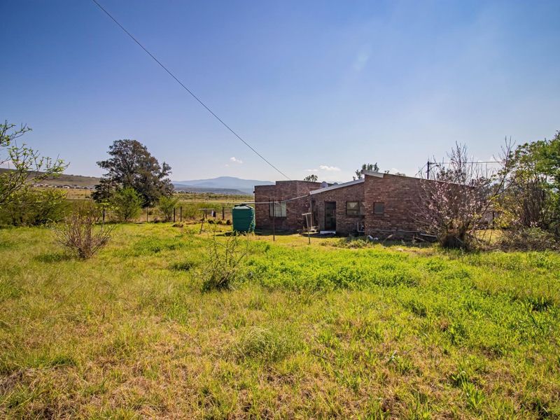 Rear view of a face brick house set on a large, undeveloped plot with a water storage tank and mountain views in the distance.