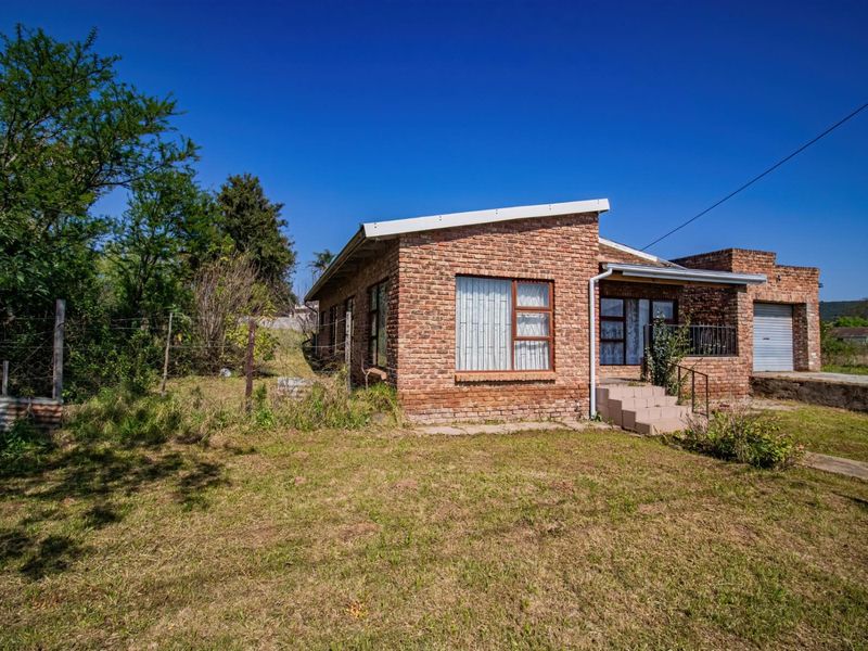 A single-story face brick house featuring a front entrance with concrete steps, a single garage, and an expansive, unmaintained garden area.
