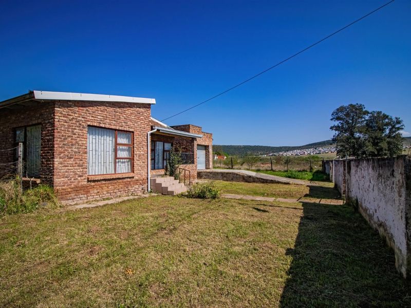 Rear view of a face brick house featuring a concrete driveway, perimeter boundary wall, and expansive garden space with scenic landscape views.