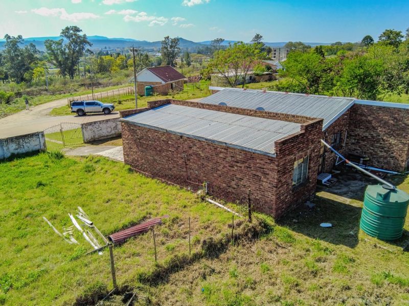 Aerial view of a face brick house featuring a corrugated metal roof, water storage tank, and surrounding grounds in a rural setting.