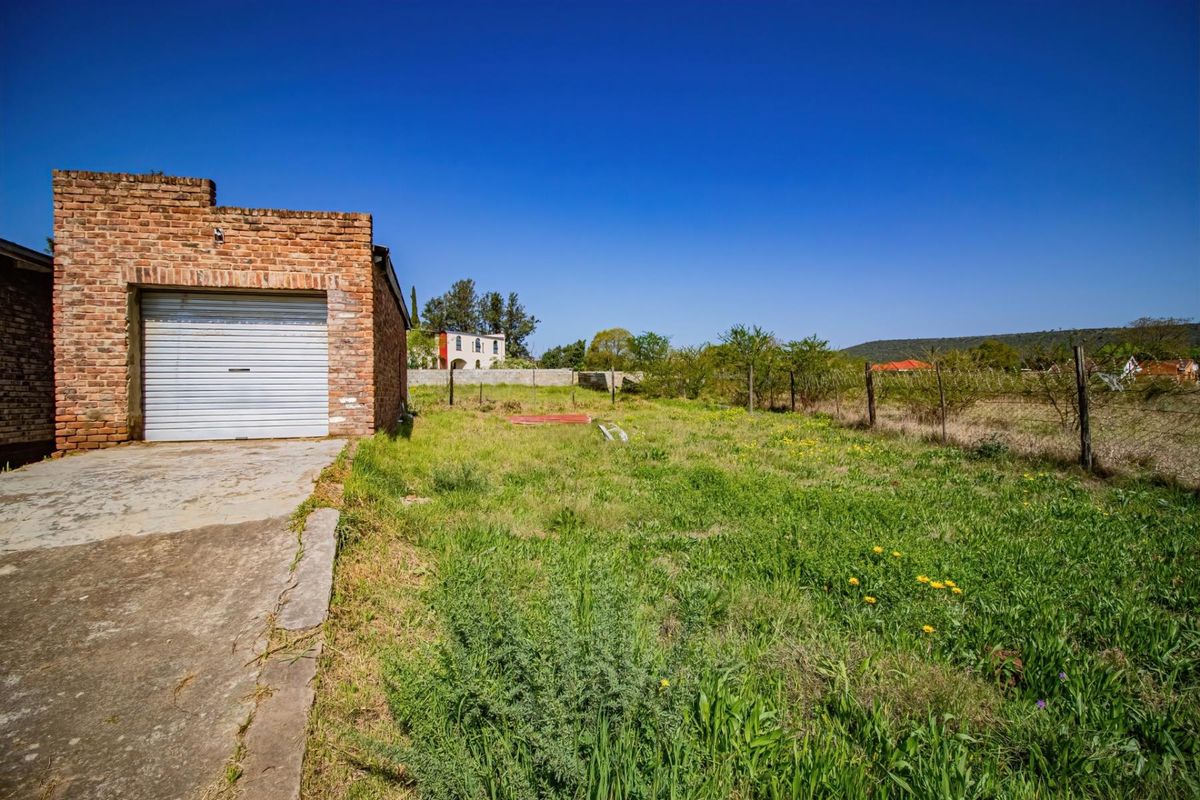 A view of the rear yard featuring a brick garage structure, concrete driveway, and expansive grass area enclosed by wire fencing.