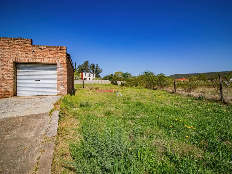 A view of the rear yard featuring a brick garage structure, concrete driveway, and expansive grass area enclosed by wire fencing.