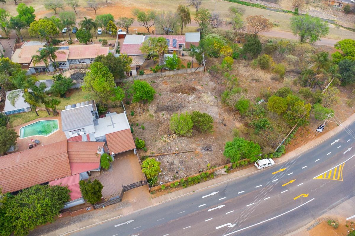 Aerial view of a vacant residential plot situated between established properties, featuring direct road access and natural vegetation.