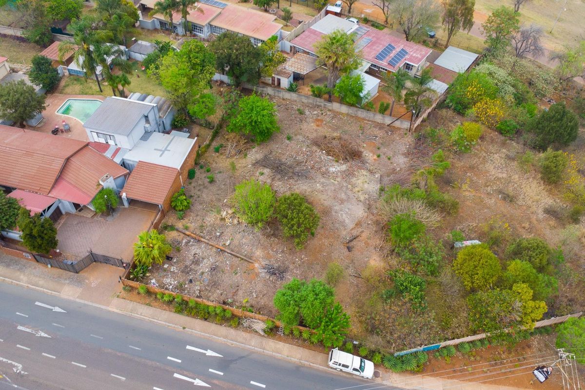 Aerial view of a vacant residential plot featuring established trees and perimeter fencing, situated in an established neighborhood with direct street access.
