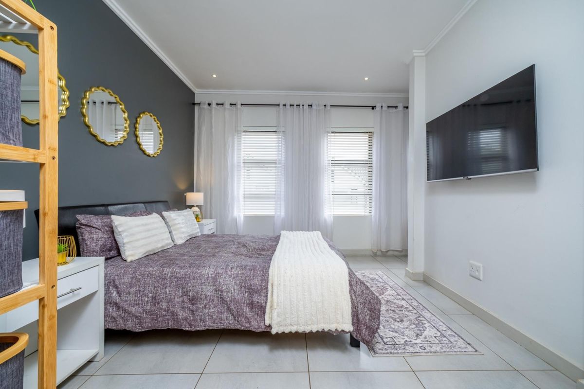 A well-maintained bedroom featuring tiled flooring, recessed downlighting, and dual windows with venetian blinds, creating a bright and functional living space.