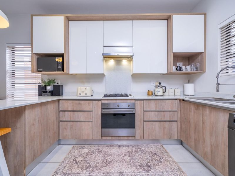 Modern U-shaped kitchen featuring light wood-grain cabinetry, white high-gloss upper cabinets, stone countertops, and integrated stainless steel appliances.