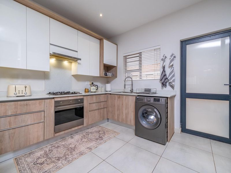 Modern kitchen featuring light wood and white cabinetry, gas hob, built-in oven, extractor fan, and tiled flooring with direct access to the exterior.