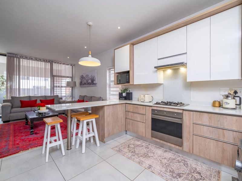 Modern open-plan kitchen and living area featuring sleek cabinetry, integrated appliances, stone countertops, and seamless access to the outdoor patio through sliding glass doors.