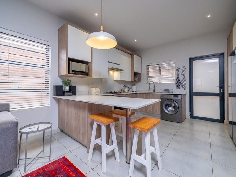 Modern kitchen featuring light wood-tone cabinetry, stone countertops, integrated appliances, and a breakfast bar, complemented by neutral tiled flooring and recessed lighting.