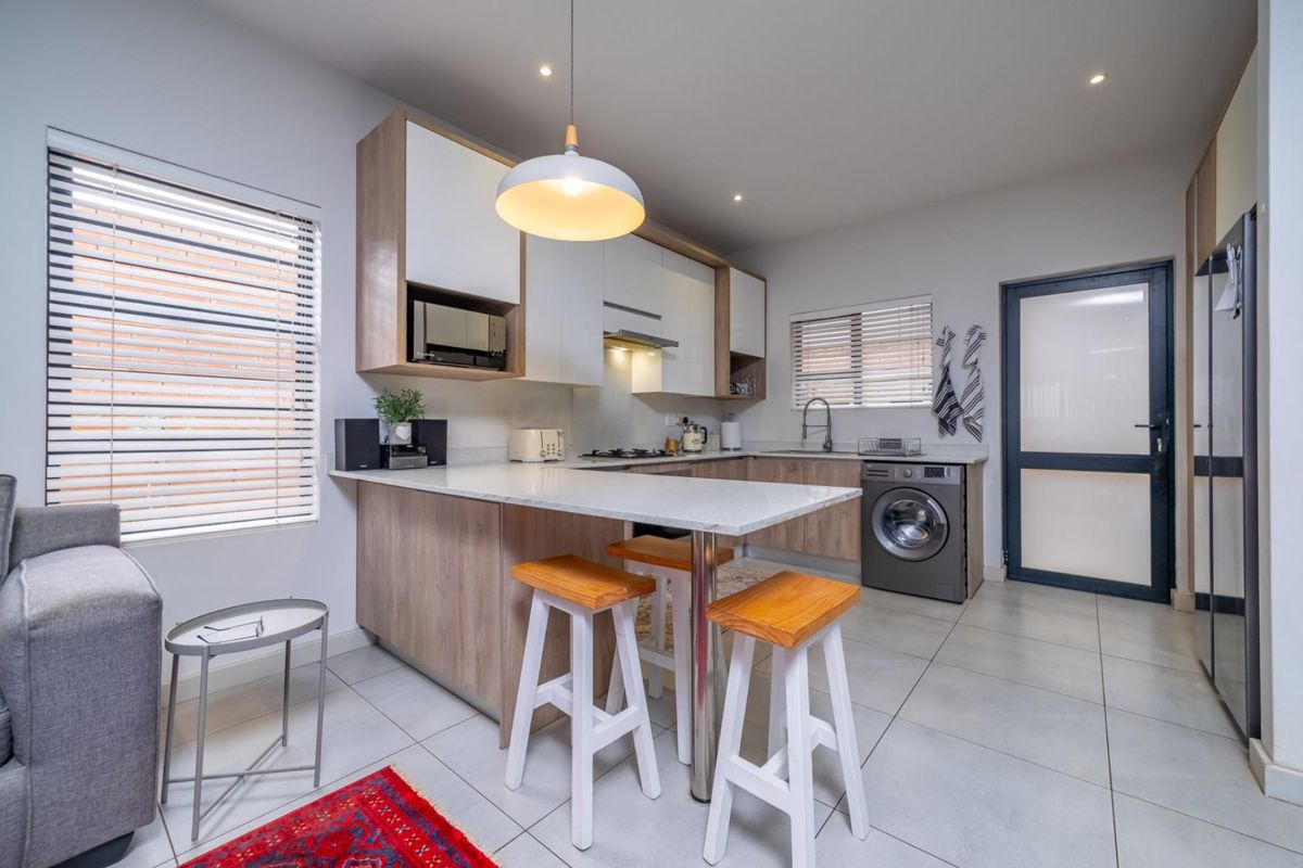 Modern kitchen featuring light wood-tone cabinetry, stone countertops, integrated appliances, and a breakfast bar, complemented by neutral tiled flooring and recessed lighting.