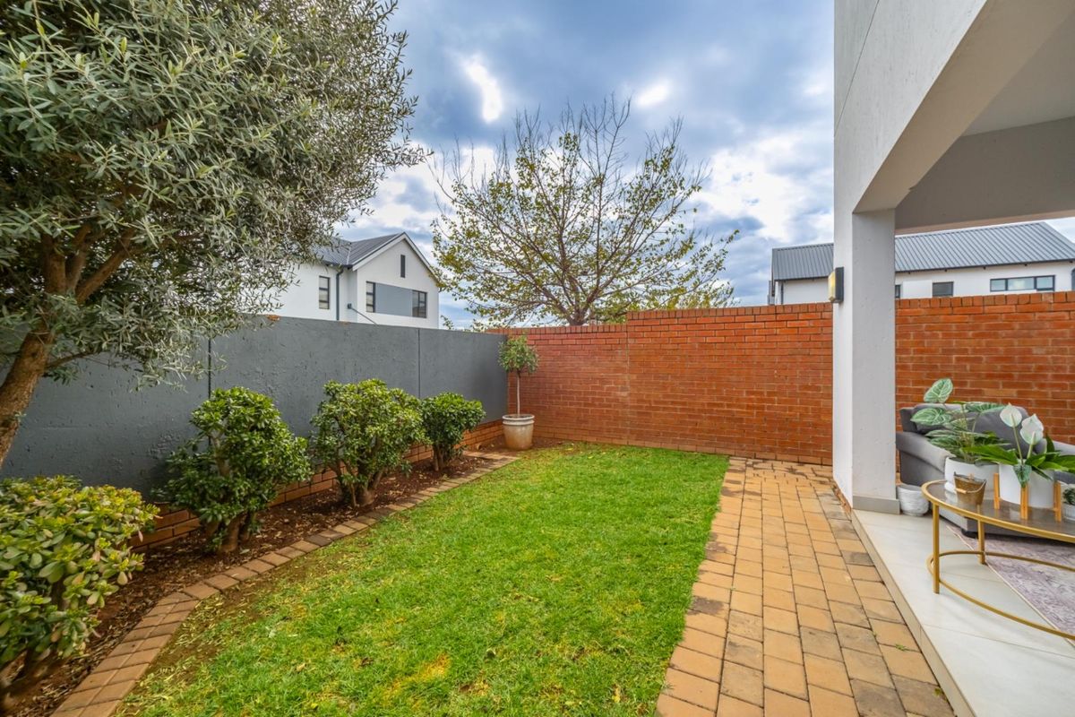 A private rear garden featuring a paved patio area, a small lawn, and a combination of brick and painted masonry boundary walls.