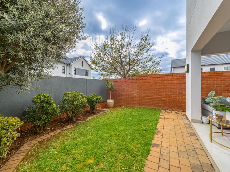 A private rear garden featuring a paved patio area, a small lawn, and a combination of brick and painted masonry boundary walls.