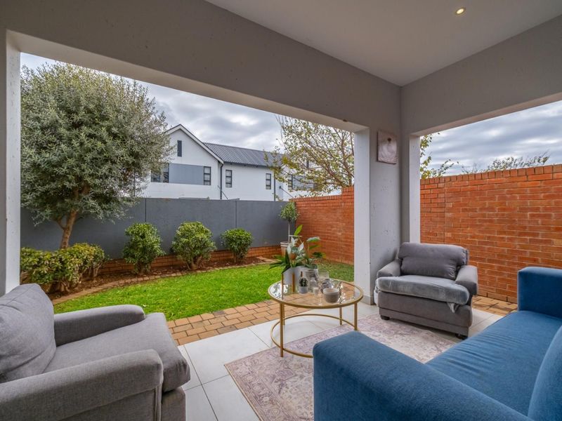 A covered patio area featuring tiled flooring and recessed lighting, overlooking a private garden with brick and concrete boundary walls.
