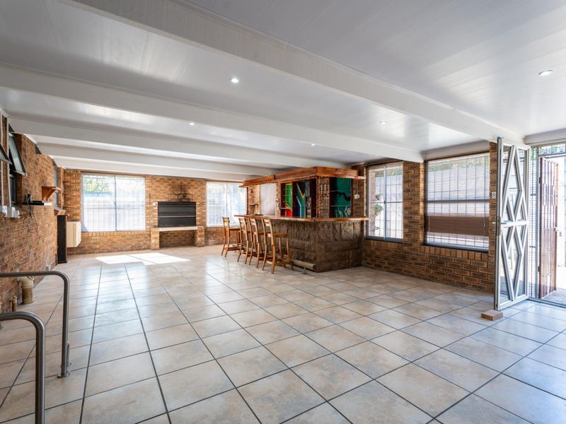 Spacious covered patio featuring a built-in bar and braai area, tiled flooring, and exposed beam ceilings, ideal for outdoor entertaining.