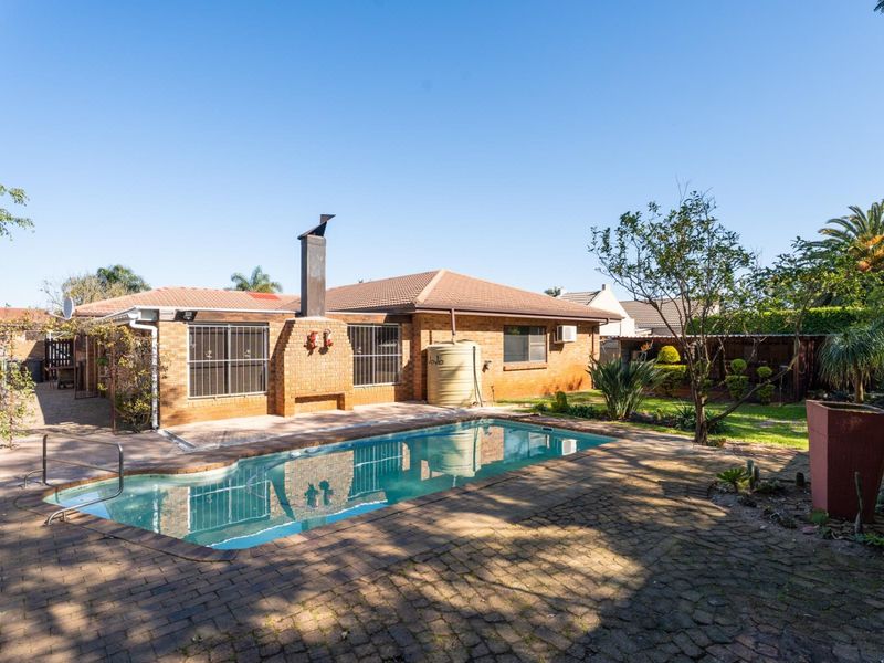 Rear exterior view featuring a swimming pool, paved patio area, brick fireplace, and a water tank set against a brick house facade.