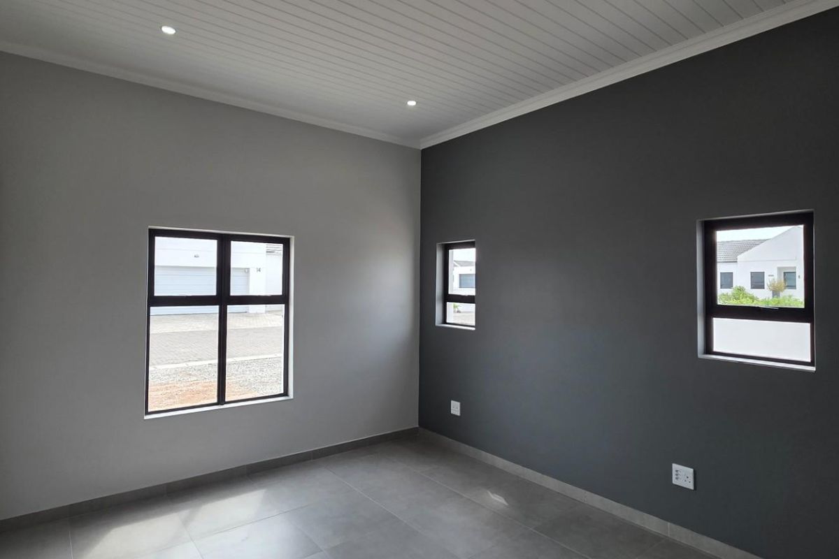 A modern, empty bedroom featuring neutral grey walls, tiled flooring, built-in cupboards, and a clean tongue and groove ceiling with recessed lighting.