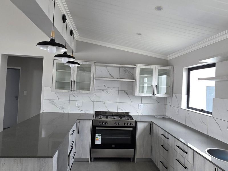 Modern kitchen featuring stone countertops, marble-look tile backsplash, gas stove, oven, and ample cabinetry with a clean, contemporary aesthetic.