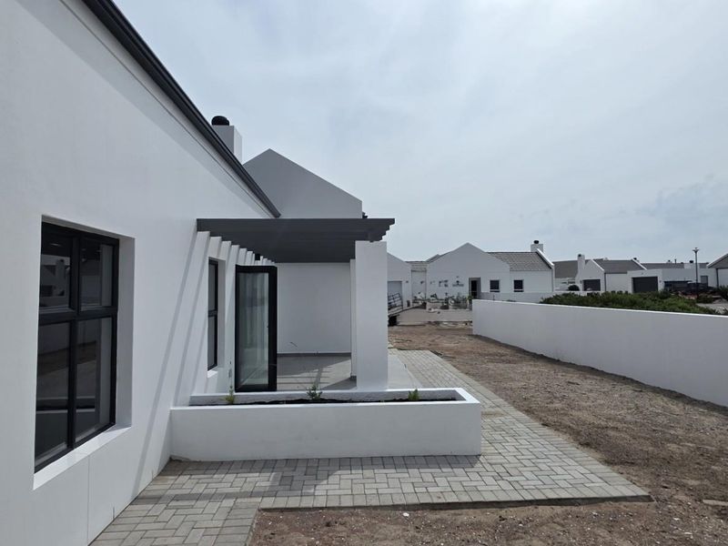 Rear exterior view featuring a paved patio area, modern pergola, and clean white boundary walls in a residential estate setting.