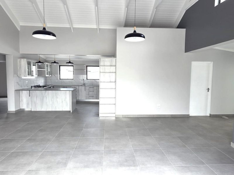 Spacious open-plan living area featuring a modern kitchen, high exposed beam ceilings, tiled floors, and a built-in brick fireplace.