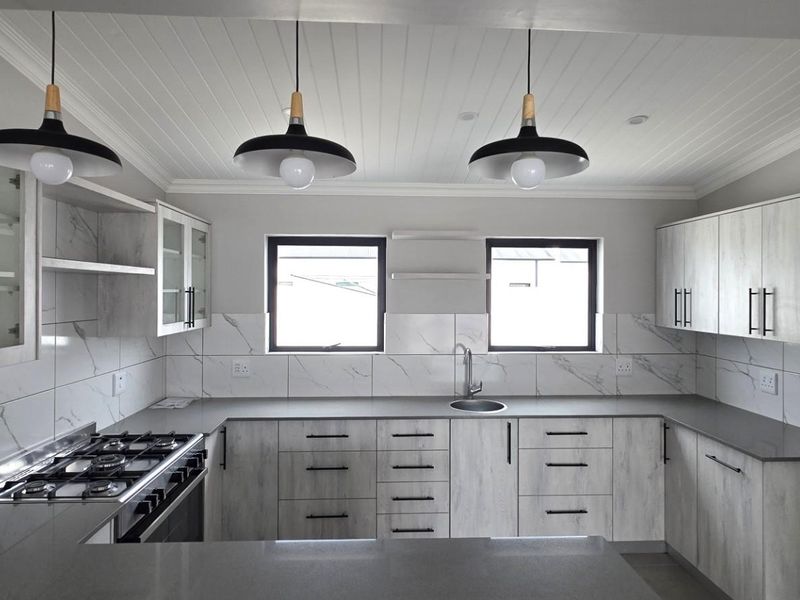 Modern kitchen featuring light wood-grain cabinetry, marble-look tiled backsplash, quartz countertops, gas hob, and stylish pendant lighting in a clean, contemporary layout.