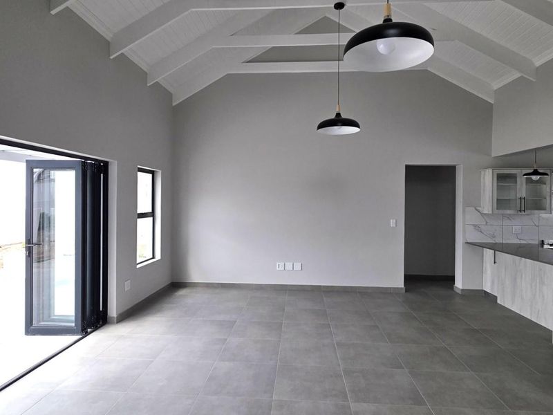 Spacious open-plan living area featuring a vaulted ceiling with exposed rafters, modern tiled floors, and seamless access to the patio through bi-fold doors.