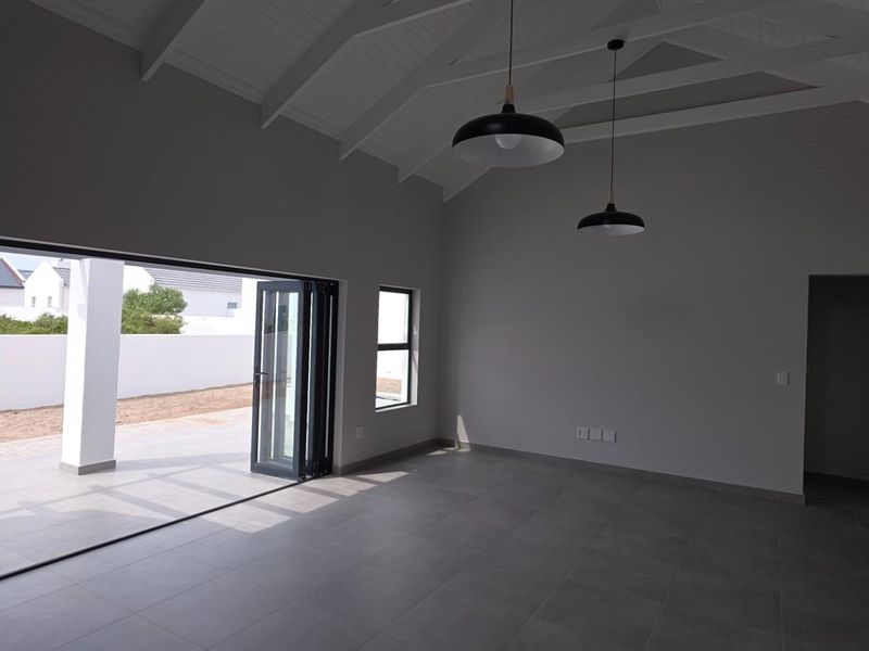 Spacious open-plan living area featuring vaulted ceilings with exposed rafters, large bi-fold doors opening to a patio, and modern tiled flooring.