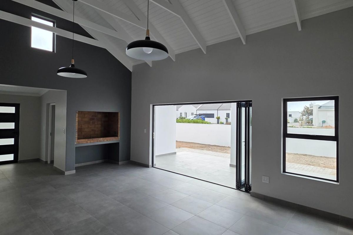 Spacious open-plan living area featuring a vaulted ceiling with exposed rafters, built-in fireplace, and large bi-fold doors opening to an outdoor patio.
