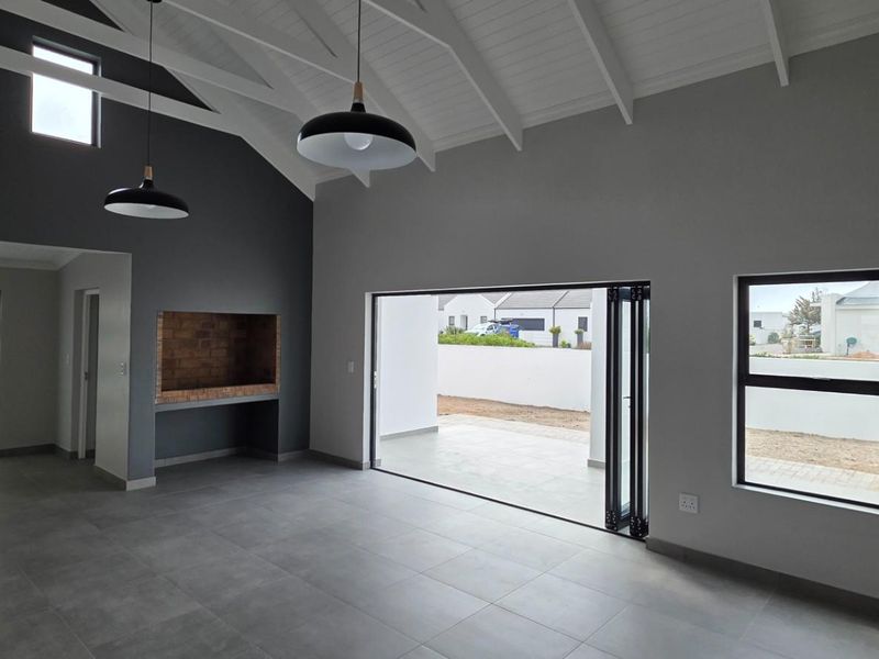 Spacious open-plan living area featuring a vaulted ceiling with exposed rafters, built-in fireplace, and large bi-fold doors opening to an outdoor patio.